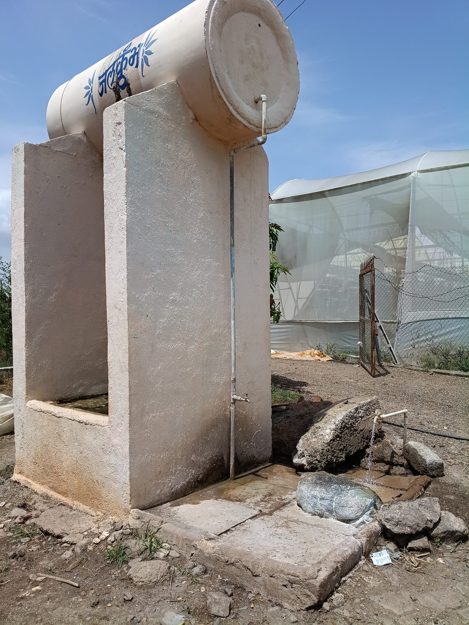 A water tank and tap beside the polyhouse at the Sakori site — water, like soil, gets checked before a trial begins